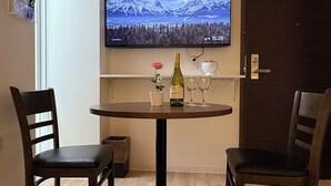 A dining area with a round table, two chairs, a bottle of wine, and a TV displaying a mountainous landscape. - Moon Base Tokyo Inn (Tokyo)