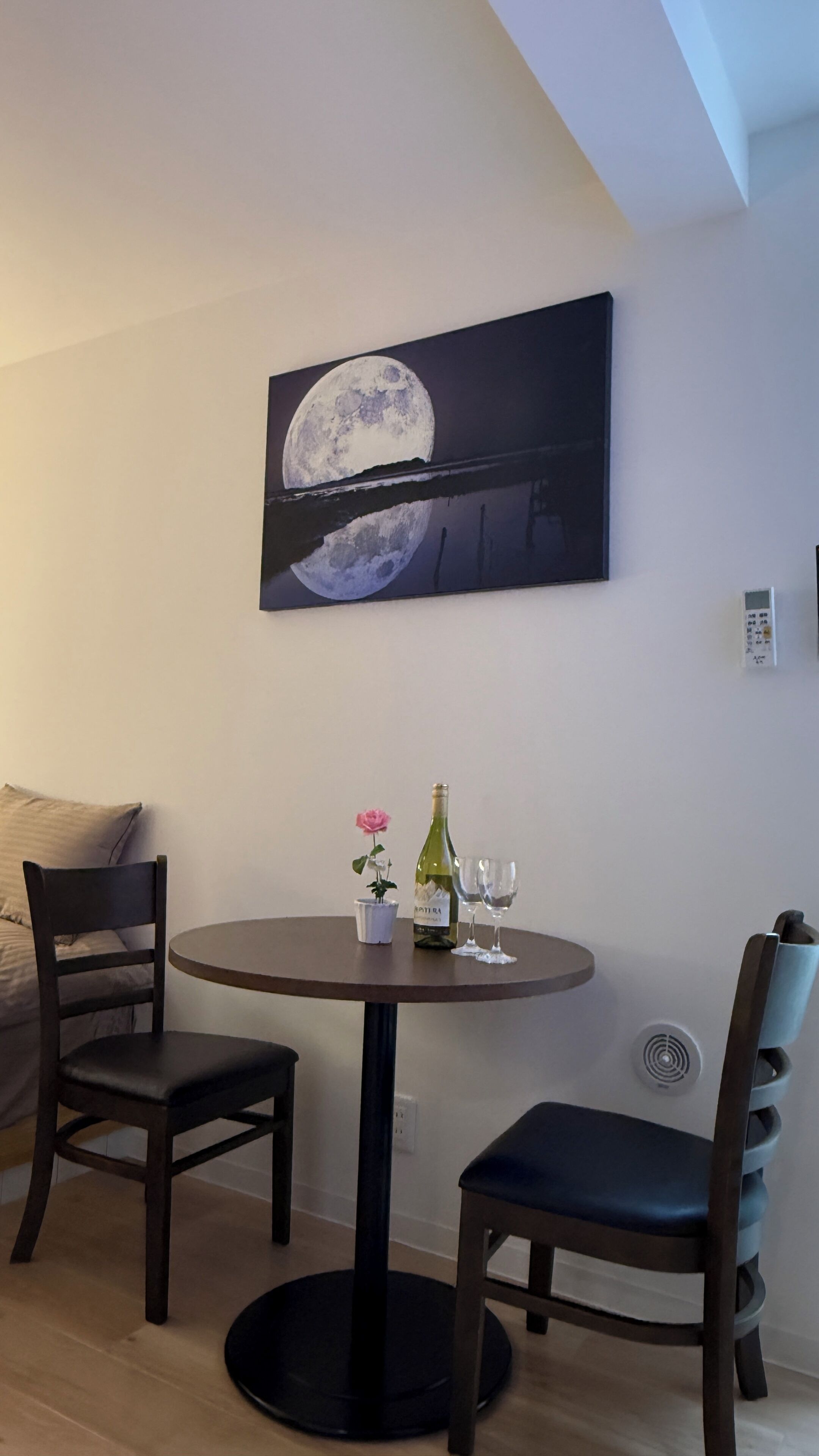 A dining area with a round table, two chairs, a bottle of wine, and a glass.