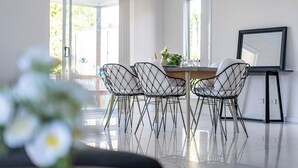 A modern dining area with a glass table, four wireframe chairs, and a large mirror on the wall. - Blanco Haus - Sweet Family Escape near Theme Parks (Pimpama)