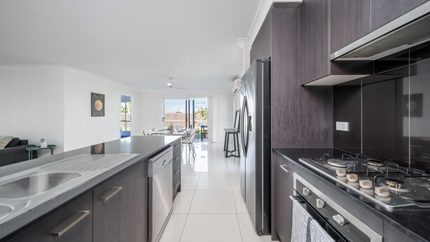 A modern kitchen with dark cabinetry, stainless steel appliances, and a large island with a sink. - Blanco Haus - Sweet Family Escape near Theme Parks (Pimpama)