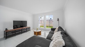 A modern living room with a large flat-screen TV, a dark sofa, a wooden console table, and a round wooden coffee table. - Blanco Haus - Sweet Family Escape near Theme Parks (Pimpama)