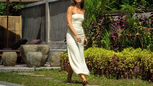 A woman in a white dress walking in a garden with palm trees and a concrete wall. - Grita Apsari Lodge Ubud (Tegallalang)