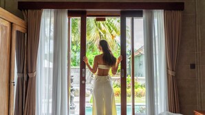 A room with a bed, a view of a pool, and a statue outside. - Grita Apsari Lodge Ubud (Tegallalang)