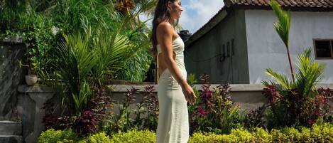 A woman standing by a pool with palm trees and a house in the background.