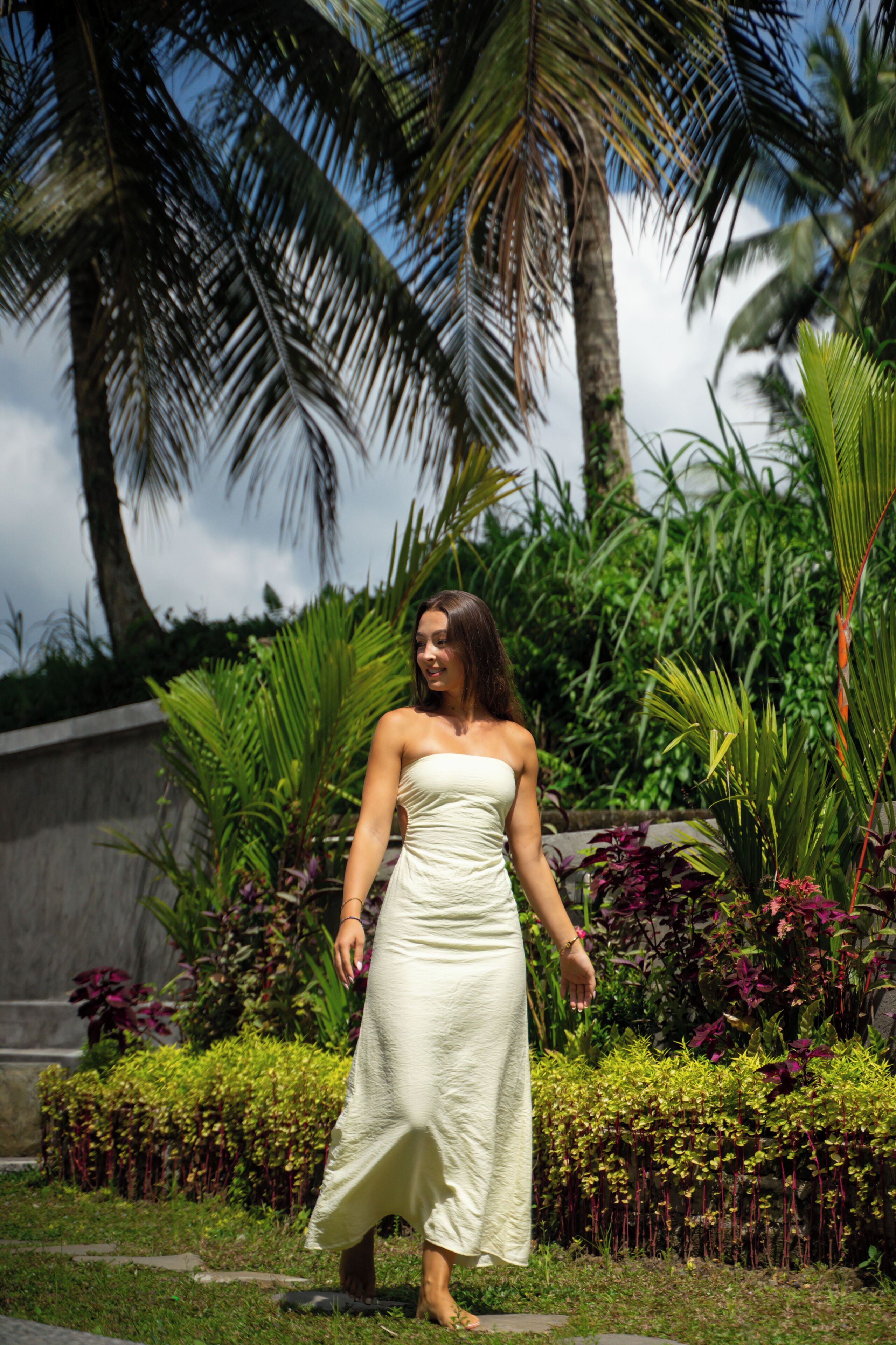 A person standing in a garden with palm trees and various plants.
