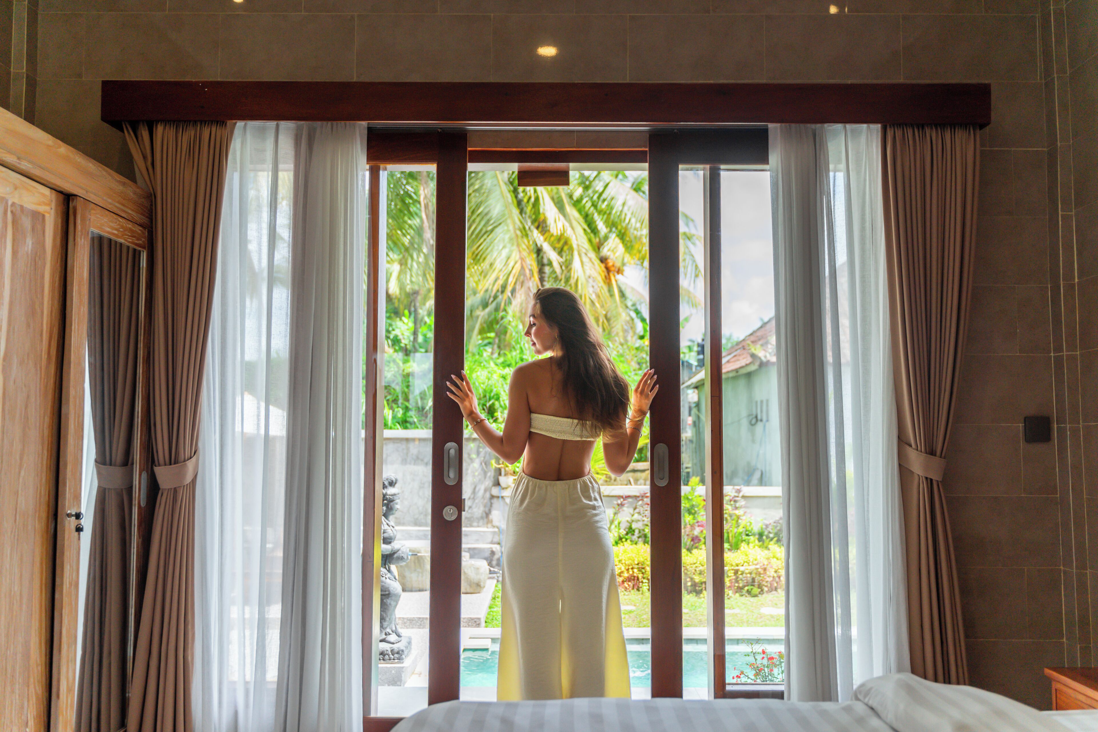 Una habitación con cama, puerta corredera de vidrio que da a una piscina y cortinas en las ventanas.