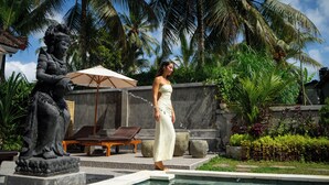 A woman in a white dress standing by a pool with a statue and lounge chairs in a tropical setting. - Grita Apsari Lodge Ubud (Tegallalang)
