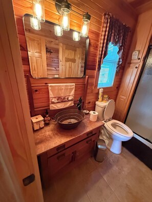 Ein kleines Badezimmer mit einem Holzkosmetikschrank, einem Spiegel, einem Waschbecken, einer Toilette und einem Fenster mit Vorhängen.