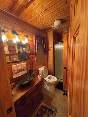A wooden cabin bathroom with a toilet, sink, and mirror.