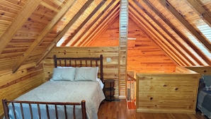 A wooden loft bedroom with a sloped ceiling, a wooden bed, a nightstand, and a dresser.