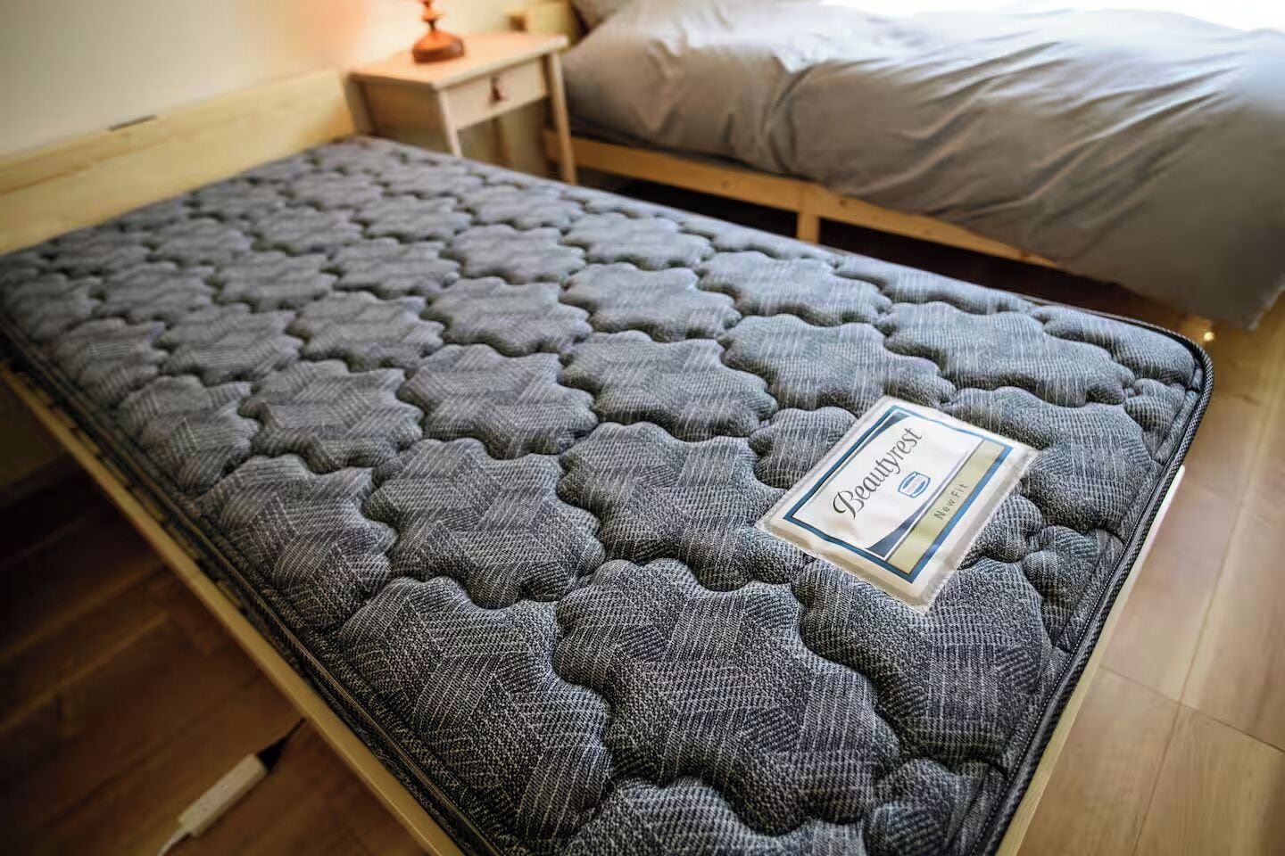 A single bed with a grey mattress and a label indicating it is a Beautyrest brand.