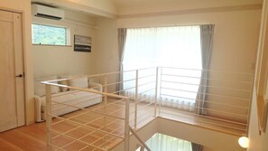A room with a wooden floor, a white sofa, a window with curtains, and a white railing. - Art Stay Hakone (Hakone)