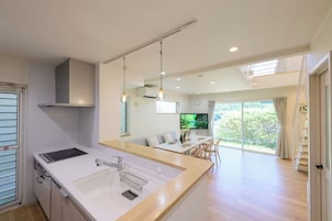 Una cocina moderna con una isla central, un área de comedor con televisor y vistas a la vegetación a través de amplios ventanales.