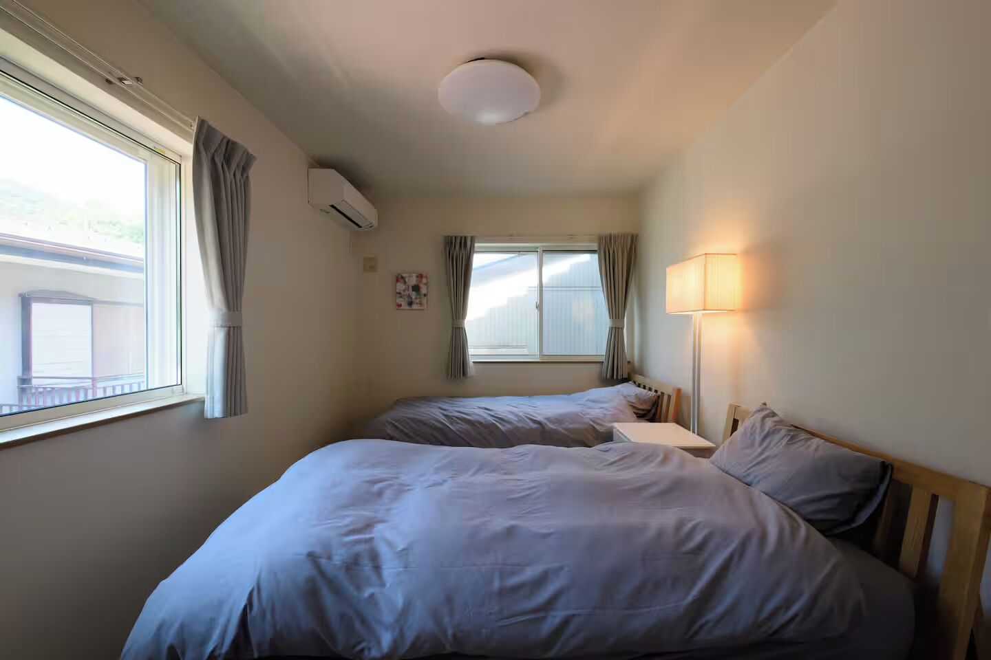 Ein Zimmer mit zwei Betten, einem Fenster, einer Klimaanlage und einer Nachttischlampe.