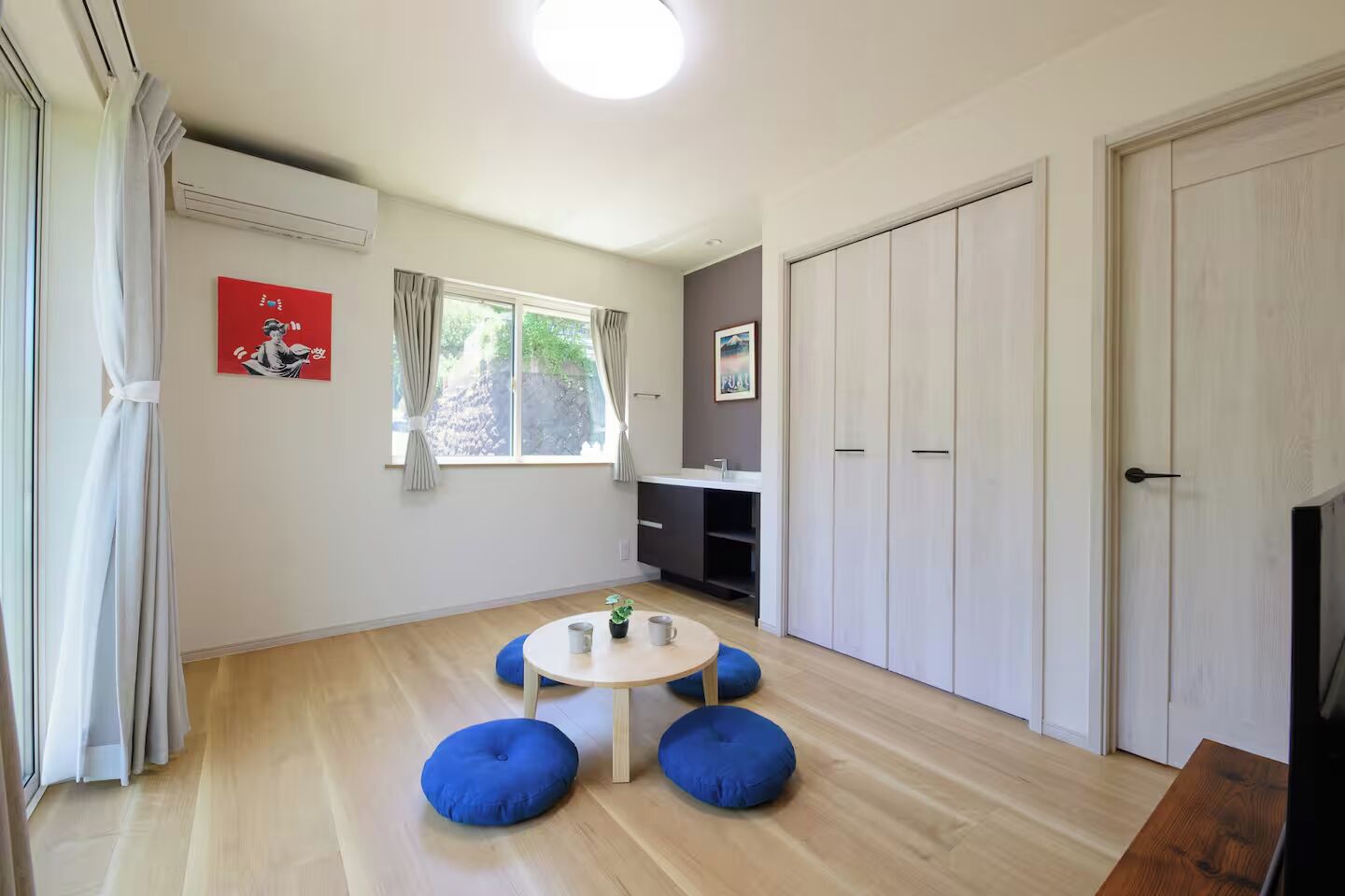 A room with a round table, blue cushions, a wardrobe, and a window with curtains.