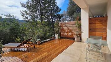 Une terrasse en bois avec un espace salon, des plantes en pot et une vue sur les arbres et les montagnes.
