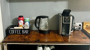 A coffee bar with a vintage clock, a coffee grinder, a kettle, and a coffee maker. There are also jars of coffee creamer and a coffee-themed sign. - Historic Downtown Apt with hot tub-walk downtown (Ocala)