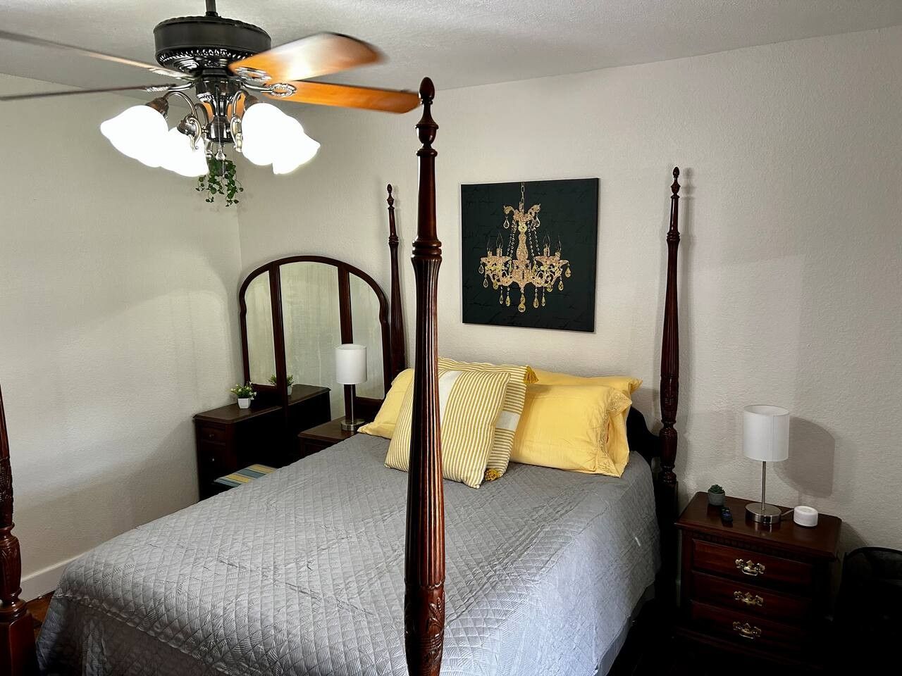 Un letto a baldacchino con ventilatore a soffitto, un comodino con lampada e un quadro appeso al muro.