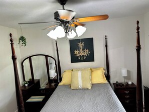 A bedroom with a four-poster bed, a ceiling fan, a chandelier, a bedside table with a lamp, and a mirror. - Morgan House | Historic Suite with Hot Tub Downtown (Ocala)