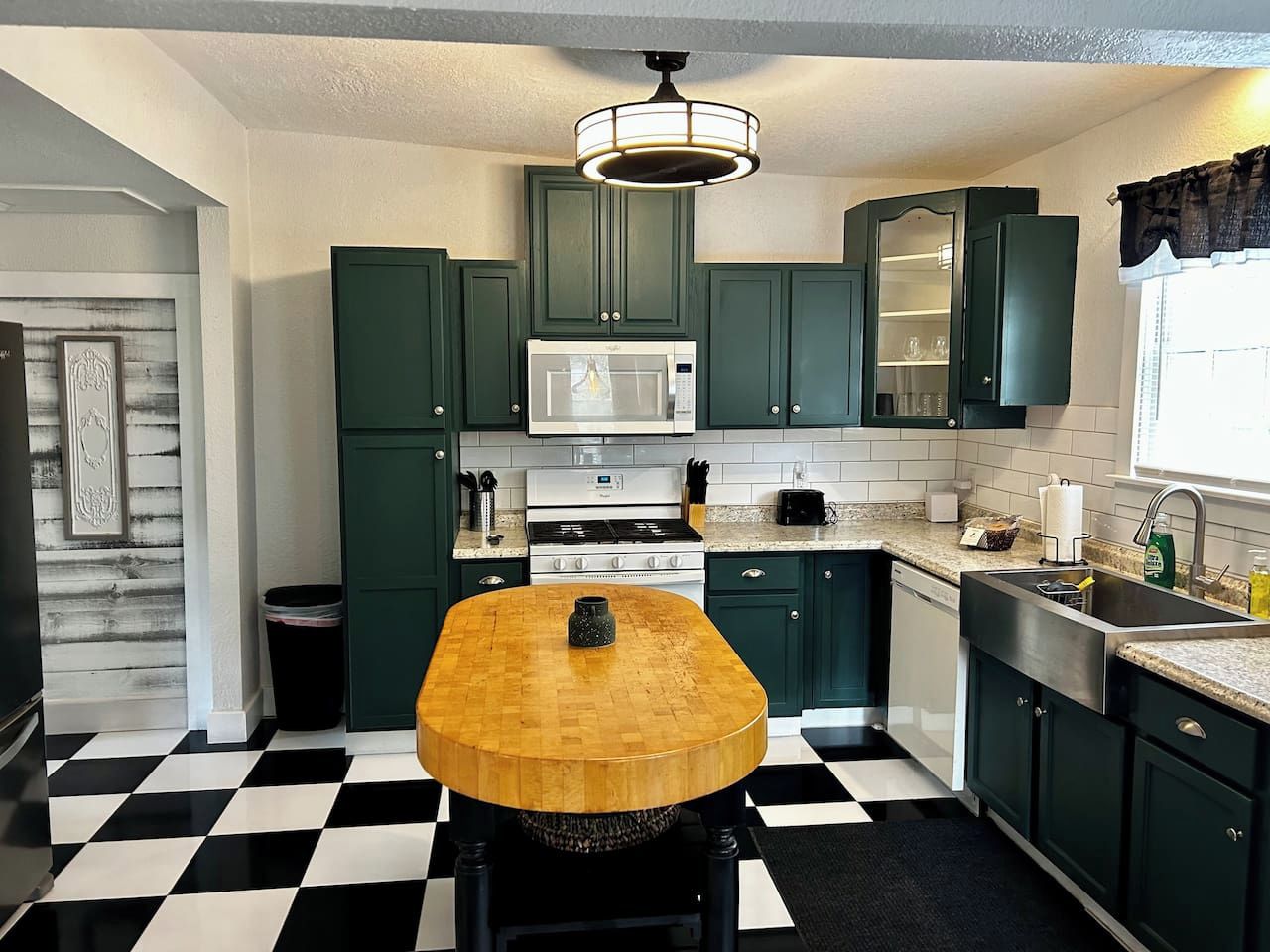 A kitchen with green cabinets, a wooden table, a microwave, and a black and white checkered floor.