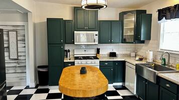 A kitchen with green cabinets, a wooden table, a microwave, and a black and white checkered floor.