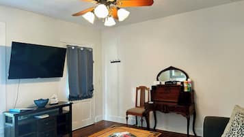 A living room with a television, a wooden coffee table, a piano, and a ceiling fan.