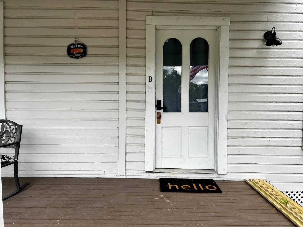 A white wooden porch with a white door, a bench, a 'hello' mat, and a sign that reads 'Farm Fresh.'