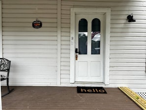 A white wooden porch with a white door, a bench, a 'hello' mat, and a sign that reads 'Farm Fresh.'