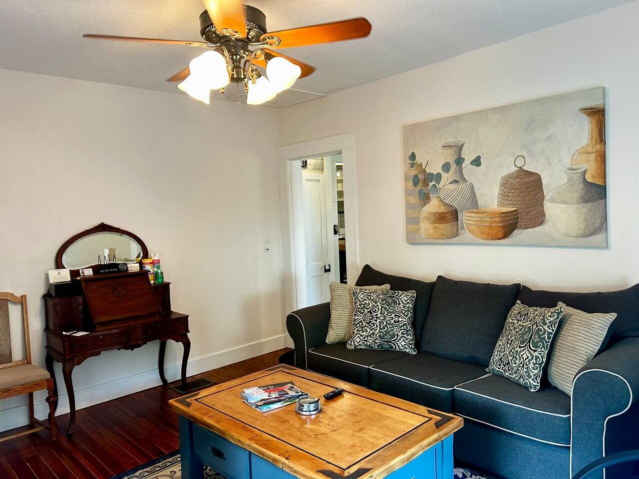 A living room with a dark blue sofa, a wooden coffee table, a wooden side table with a mirror, and a ceiling fan.