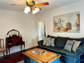 A living room with a dark blue sofa, a wooden coffee table, a wooden side table with a mirror, and a ceiling fan.