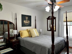 Un dormitorio con una cama con dosel, una mesita de noche con lámpara, un aparador y un espejo.