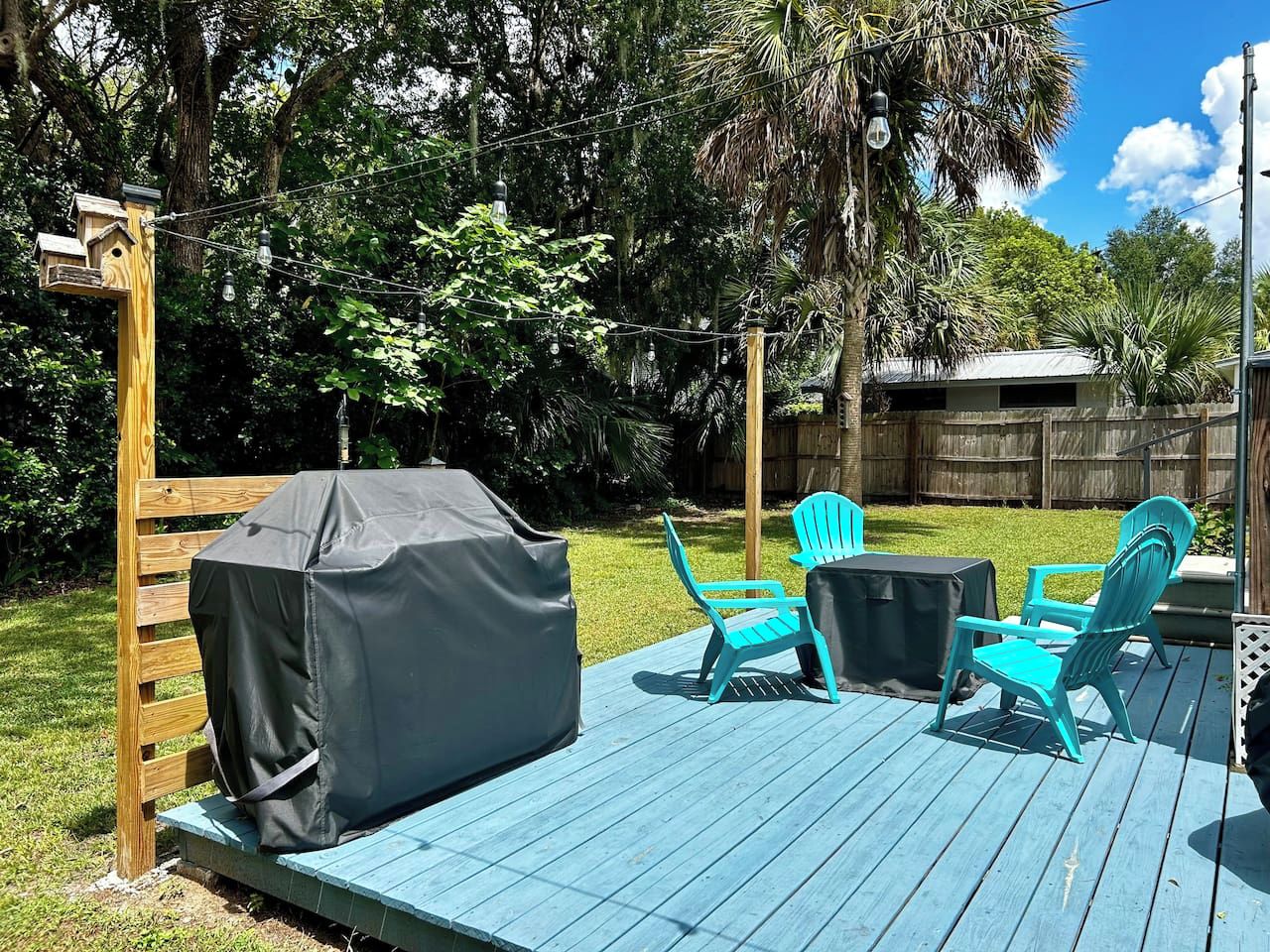 Une terrasse en bois avec un barbecue couvert, deux chaises turquoise et une table.