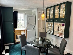 Une cuisine compacte avec une table ronde en verre, des chaises, un meuble avec des portes en verre et un luminaire suspendu.
