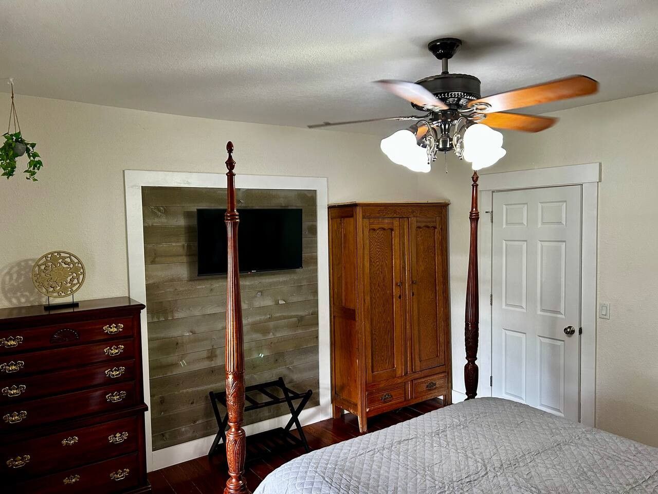 Une chambre à coucher avec un lit à baldaquin, un ventilateur de plafond, une armoire et un téléviseur fixé à un mur en bois.