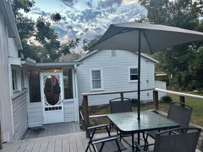 Une terrasse avec une table et des chaises, un espace abrité et une maison avec une porte et des fenêtres.