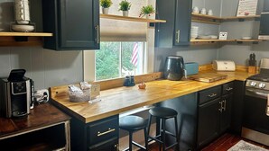 A compact kitchen with dark cabinets, a wooden countertop, a coffee maker, a toaster, and a small window with plants. - Historic Downtown Apt with hot tub-walk downtown (Ocala)