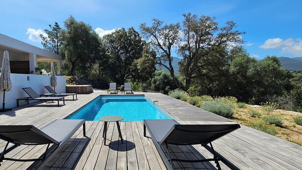 A modern outdoor pool area with wooden decking, lounge chairs, and a clear view of the surrounding landscape.