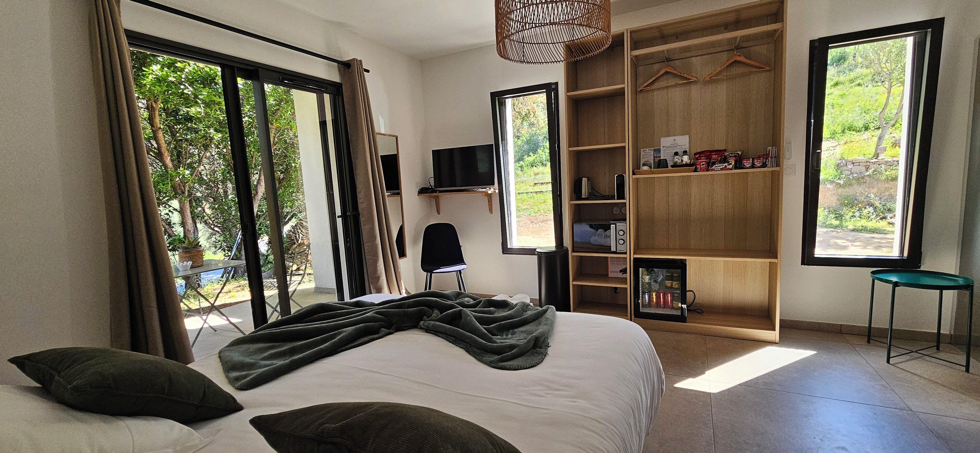 A bedroom with a bed, a TV, a wardrobe, and a view of greenery outside.