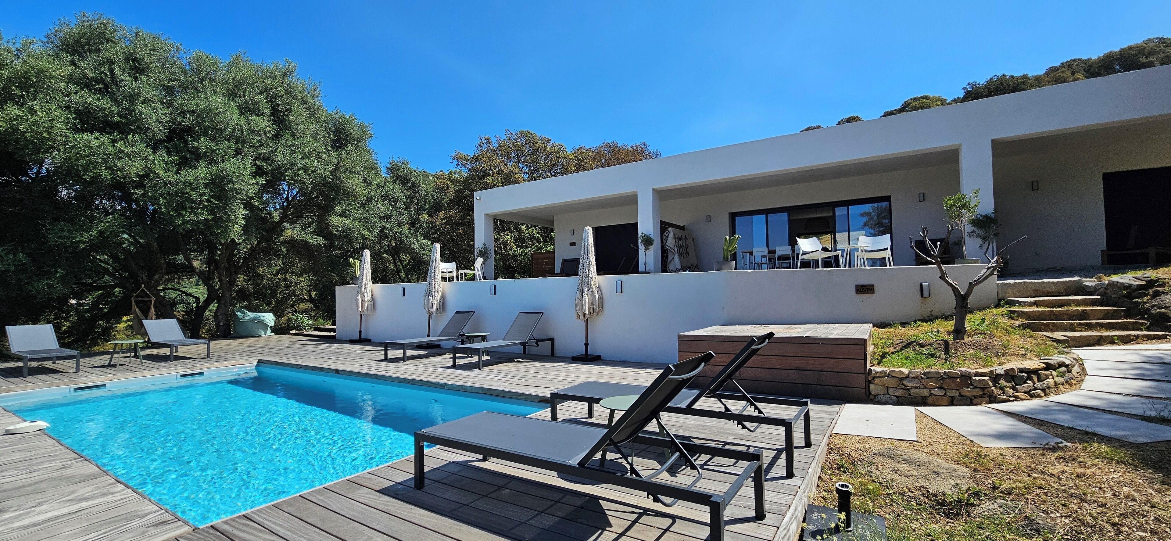 Una casa moderna con piscina, mobiliario exterior y un camino de piedra.