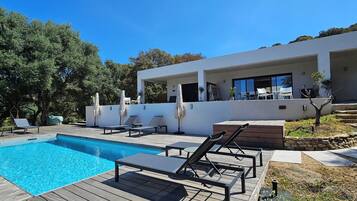 Una casa moderna con piscina, mobiliario exterior y un camino de piedra.