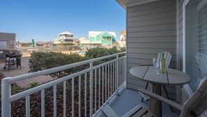 Un balcón con una mesa y sillas, vista a una piscina y casas al fondo.
