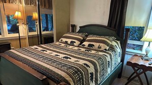 A bed with a quilt featuring animal prints, a bedside table with a lamp, and a mirror reflecting the room. - Charming Log Home on acreage bordering golf course with full gym (Port Alberni)
