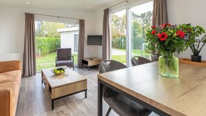 Een moderne kamer met een houten tafel, een bank, een televisie en een groot raam met gordijnen.