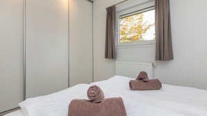 Een hotelkamer met een bed, twee handdoeken, een raam met gordijnen en een radiator.