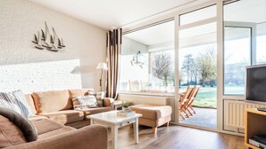 Una sala de estar moderna con un ventanal grande, un conjunto de sofás, una mesa de centro y un televisor sobre un mueble.