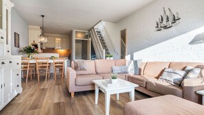 Una sala de estar moderna con un conjunto de sofás, una zona de comedor con sillas de madera y una cocina al fondo.