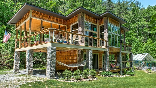 Een houten vakantiehuis met meerdere verdiepingen, een balkon, stenen fundering en een tuinhuis.