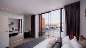 A modern hotel room with a large bed, a balcony with a view of the city, and a sliding door leading to another room. - Heart of Hobart | CBD Apartment & Parking (Hobart City)