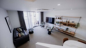A modern living room with a sofa, armchairs, a coffee table, a TV, and a bookshelf. - Heart of Hobart | CBD Apartment & Parking (Hobart City)