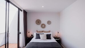 A bedroom with a bed, two bedside tables, a window with curtains, and wall decorations. - Heart of Hobart | CBD Apartment & Parking (Hobart City)